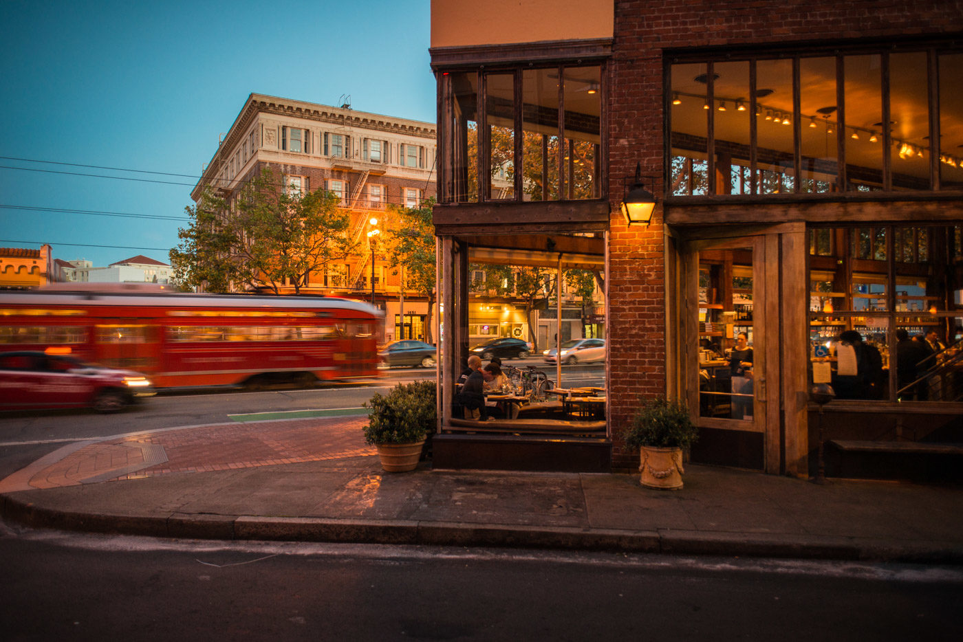 Zuni Café's glass-walled corner at Market and Rose at dusk, a red streetcar passing