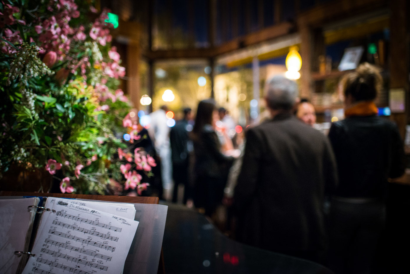 Flowers and sheet music on the piano, the dining room glowing behind